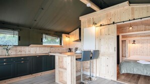 A compact kitchen with a wooden island, two bar stools, and a dining area. - Paviland - Safari Glamping Tent - Llangennith (Swansea)