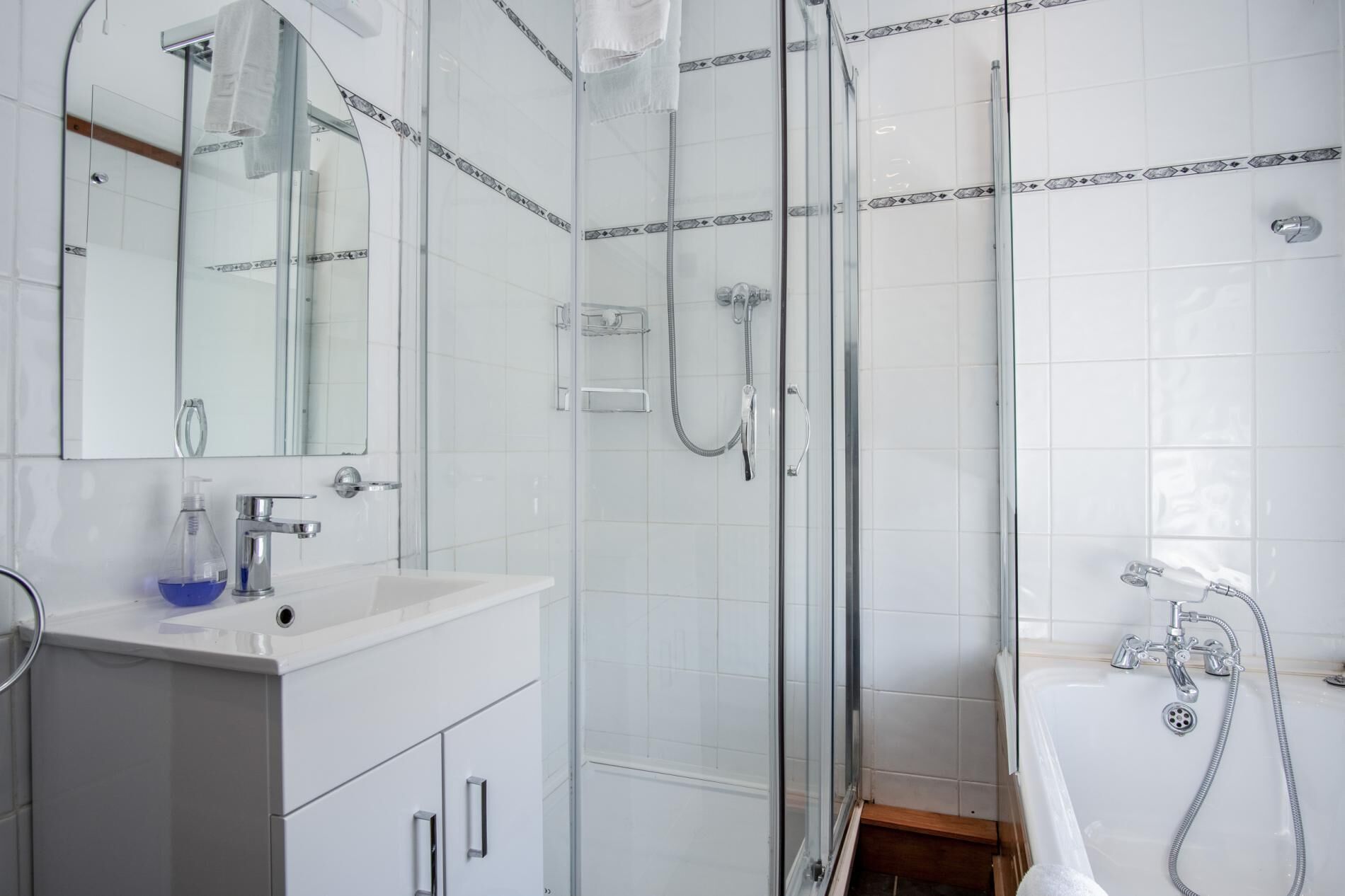 A modern bathroom with a glass-enclosed shower, a white sink with a soap dispenser, and a large mirror above the sink.
