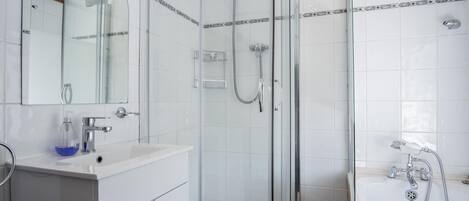 A modern bathroom with a glass-enclosed shower, a white sink with a soap dispenser, and a large mirror above the sink.
