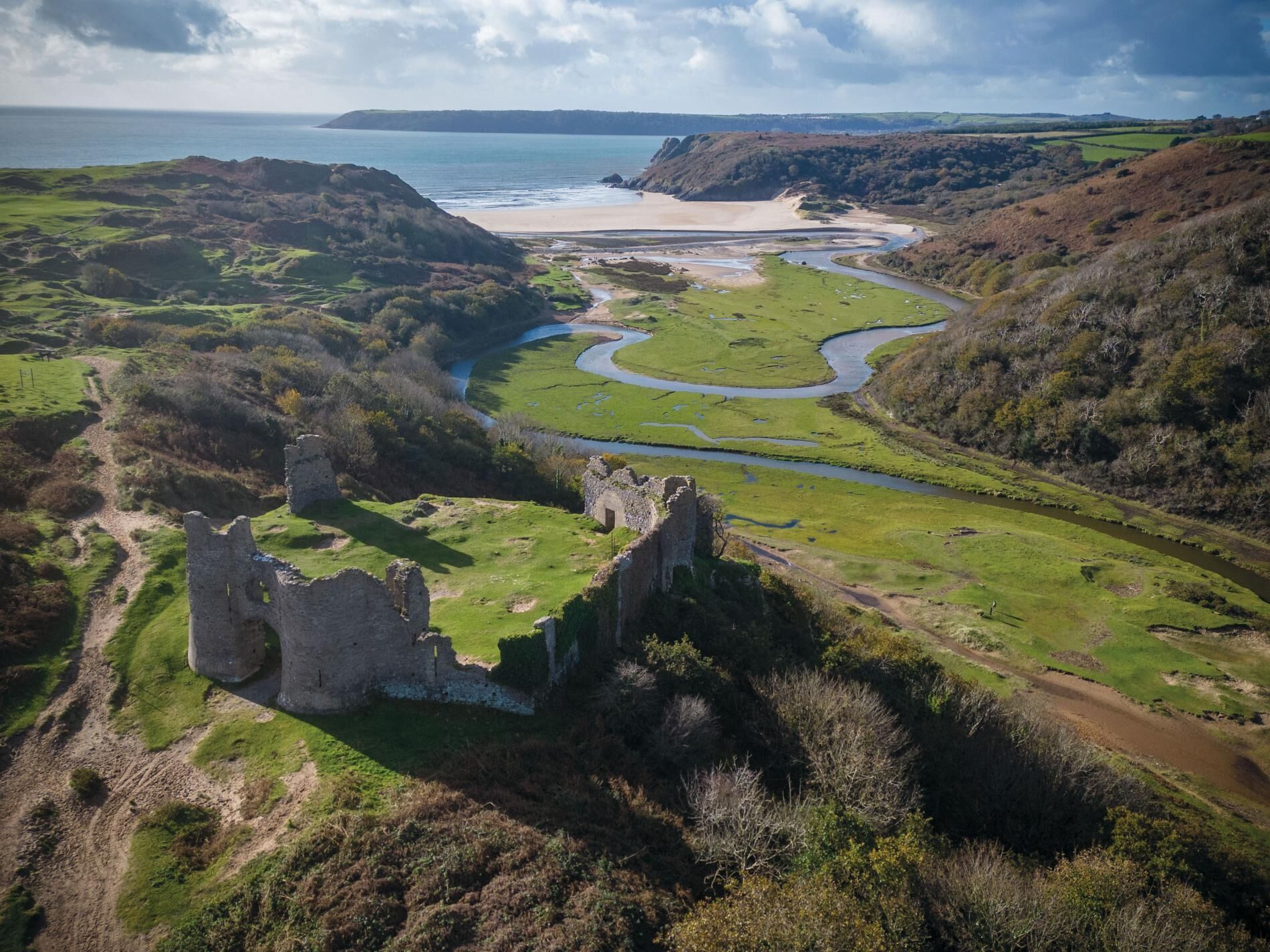 A castle ruin surrounded by green fields and a winding river.