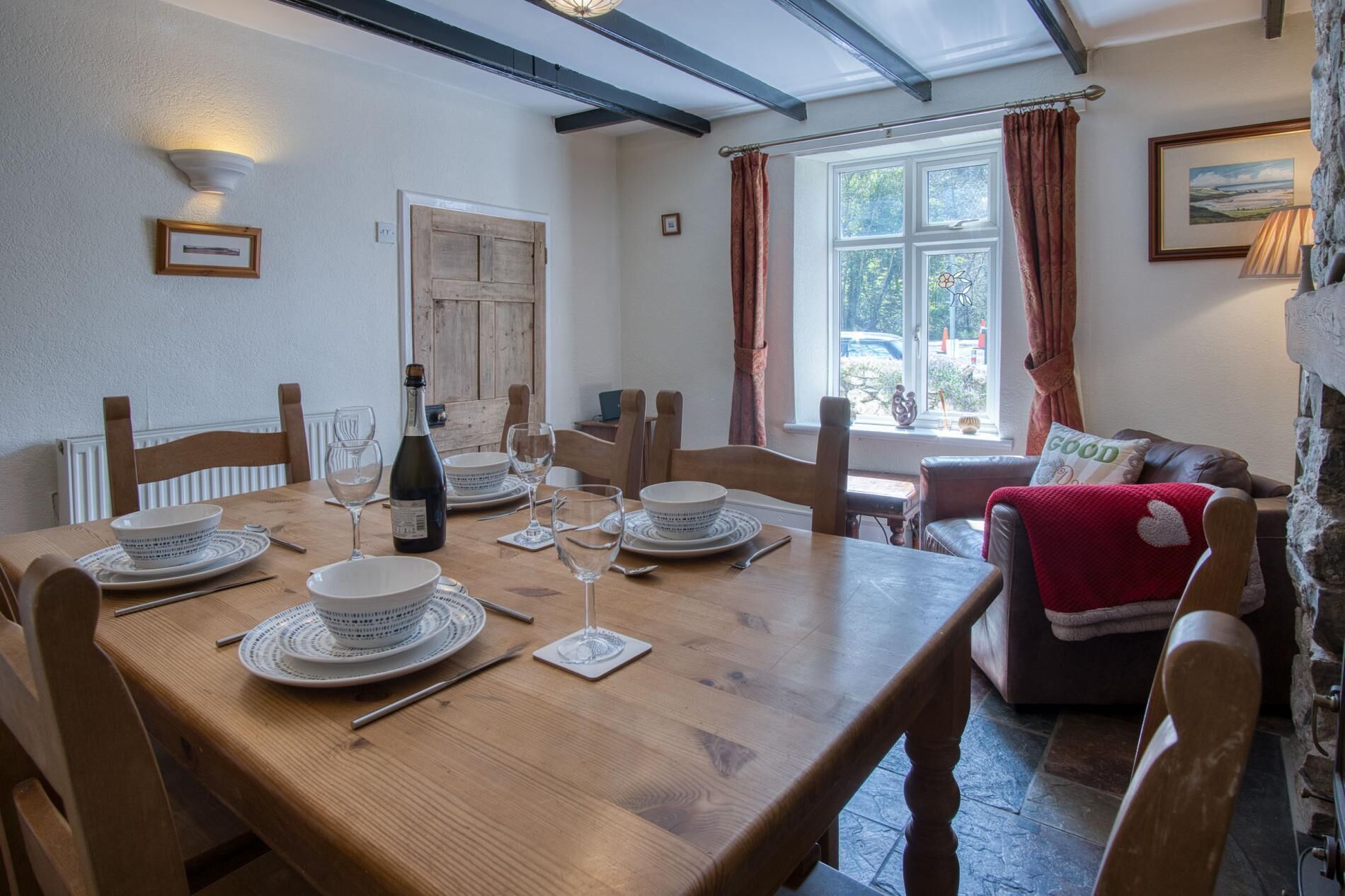 Une salle à manger avec une table en bois dressée pour quatre personnes, une bouteille de vin et une fenêtre avec des rideaux.