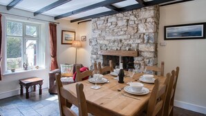A dining area with a stone fireplace, wooden table, and chairs. - Rose Cottage - 3 Bedroom Cottage - Parkmill (Swansea)