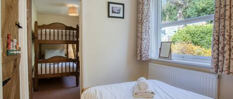 Un dormitorio con una cama individual, una ventana con cortinas, un radiador y una puerta de madera que da a una zona con literas.
