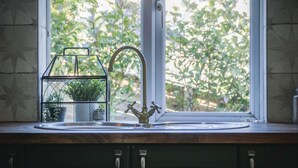 A kitchen with a window, a sink, and a metal rack with plants. - Taf Fechan - 3 Bedroom House - Pontsticill (Merthyr Tydfil)