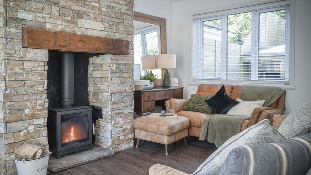A cozy living room with a stone fireplace, leather sofa, and a wooden coffee table. - Taf Fechan - 3 Bedroom House - Pontsticill (Merthyr Tydfil)