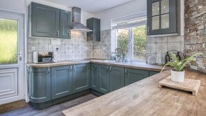 A modern kitchen with dark green cabinets, a central island, and a stone accent wall. - Taf Fechan - 3 Bedroom House - Pontsticill (Merthyr Tydfil)