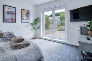 A bedroom with a bed, a desk, a TV, and a window with a view of a garden. - Cefn Road - 3 Bedroom Bungalow - Glais (Swansea)