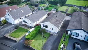 A residential area with houses having sloped roofs, a paved driveway, and a green field in the background. - Cefn Road - 3 Bedroom Bungalow - Glais (Swansea)