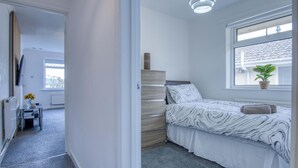 A bedroom with a bed, a window, a plant, and a desk with a vase of flowers. - Cefn Road - 3 Bedroom Bungalow - Glais (Swansea)