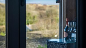 Una botella de vino y dos copas sobre una mesa junto a una ventana con vistas a un paisaje.