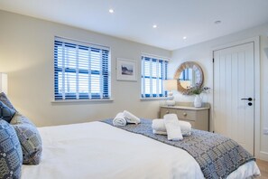 Ein Hotelzimmer mit einem großen Bett, zwei Fenstern mit Jalousien, einem Nachttisch mit Lampe, einem Spiegel und einer Tür.