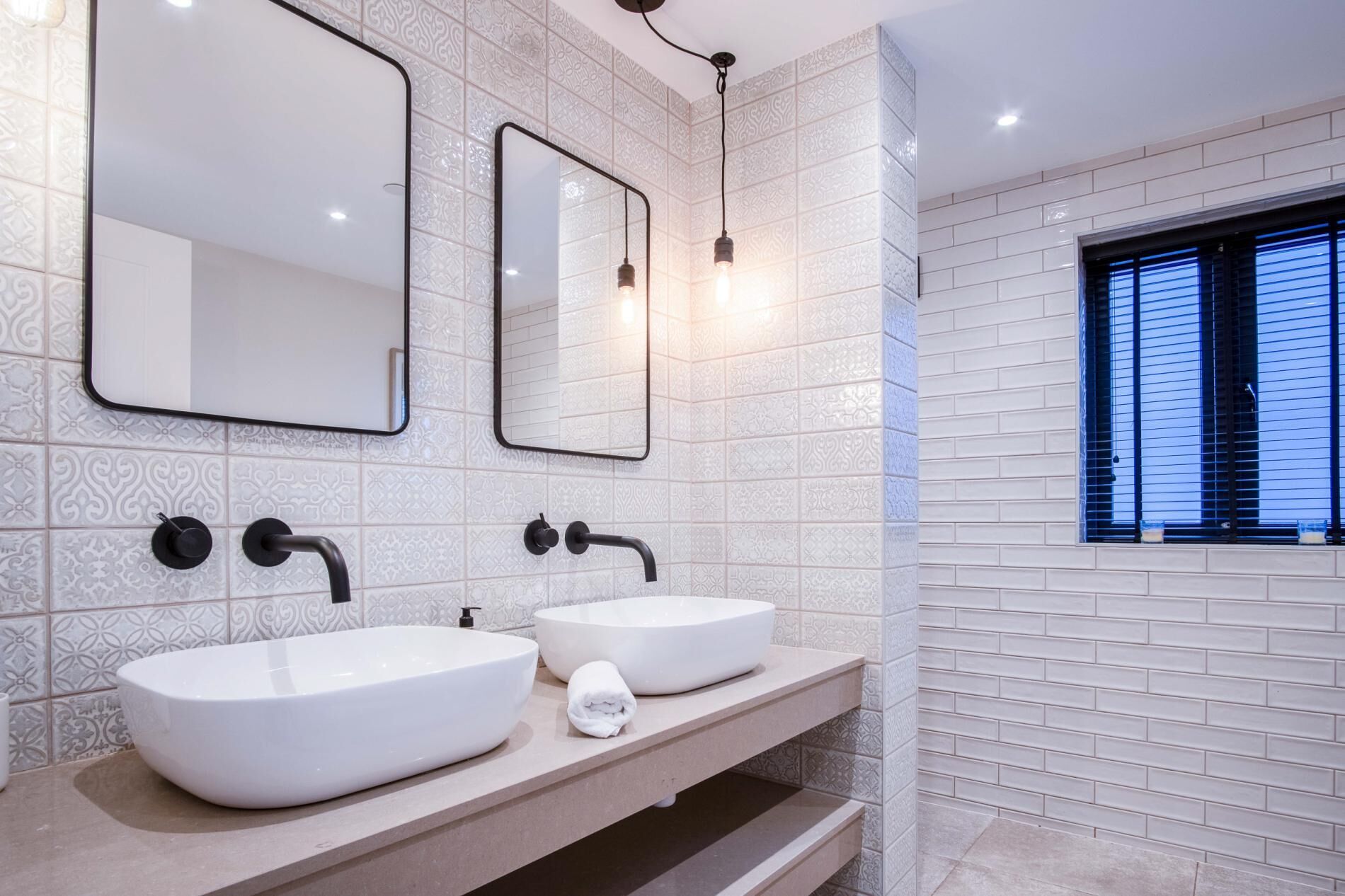 A modern bathroom with two white vessel sinks, a large mirror, and a window with blinds.