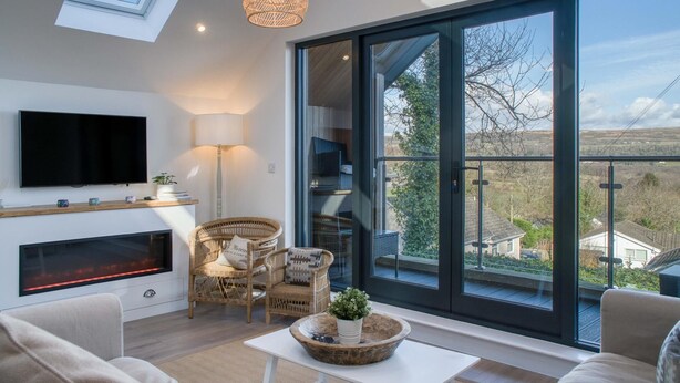 Una sala de estar moderna con chimenea, televisor y un amplio ventanal corredera que da a una vista panorámica del exterior.