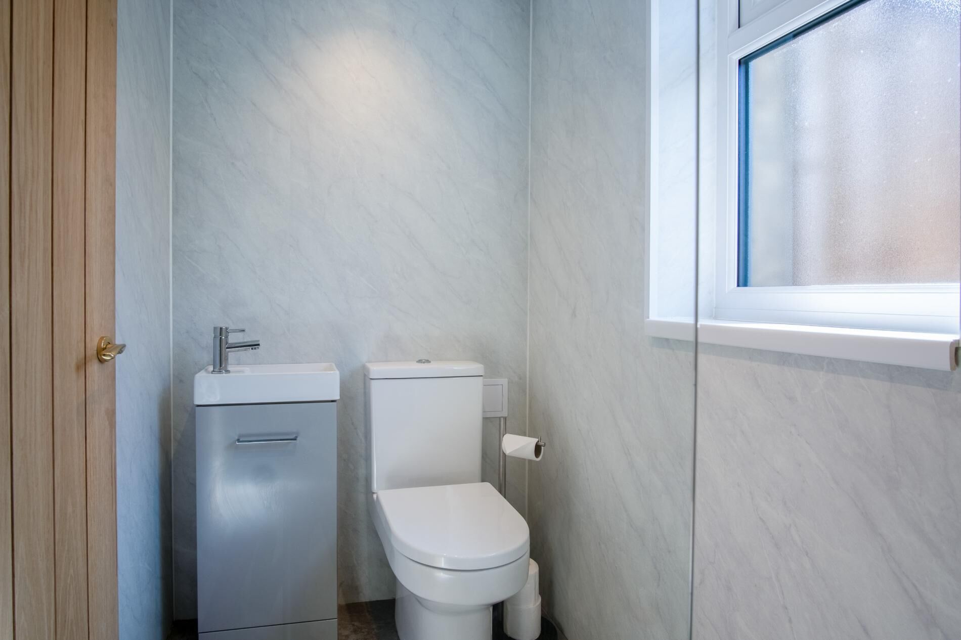 A small, modern bathroom with a toilet, sink, and window.