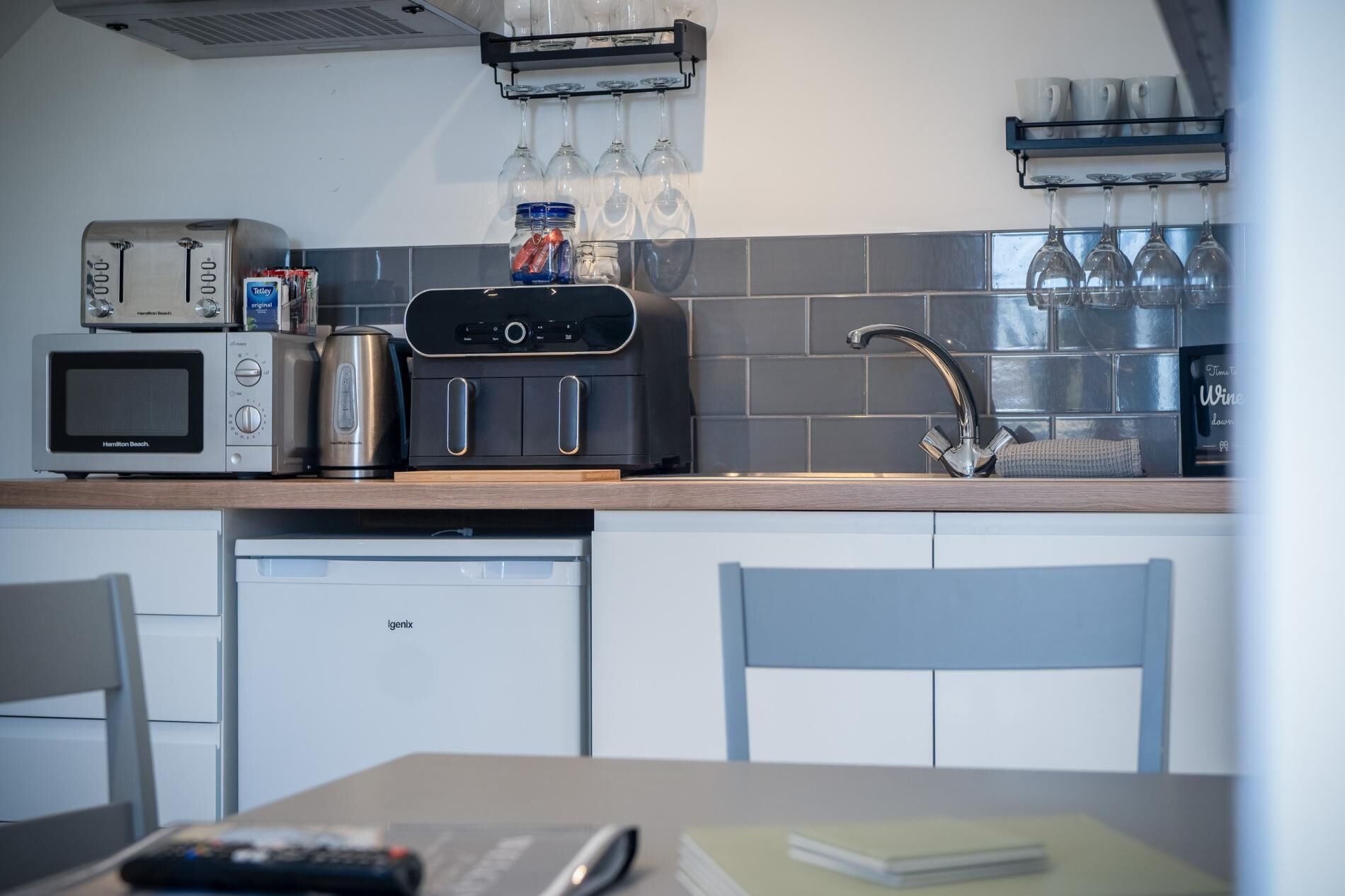 Een moderne keuken met een magnetron, broodrooster, koffiezetapparaat en een wijnkoeler. Er is een spoelbak met een kraan en een handdoek hangt aan de muur.