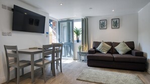 Una sala de estar moderna con un sofá, una mesa de comedor con sillas y un televisor de pantalla plana montado en la pared.