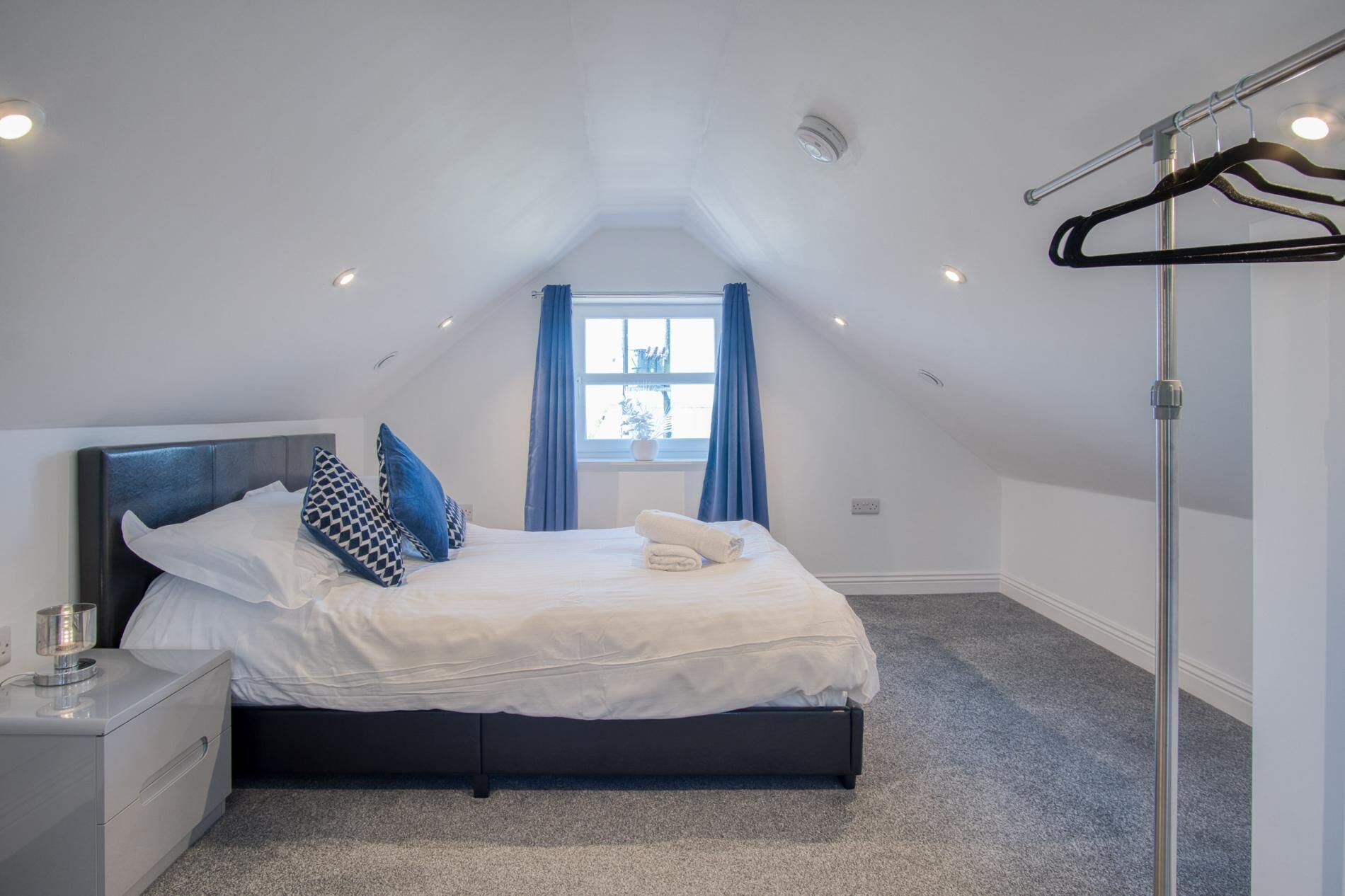 A bedroom with a bed, a bedside table, a window with curtains, and a ceiling light.
