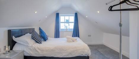 A bedroom with a bed, a bedside table, a window with curtains, and a ceiling light.