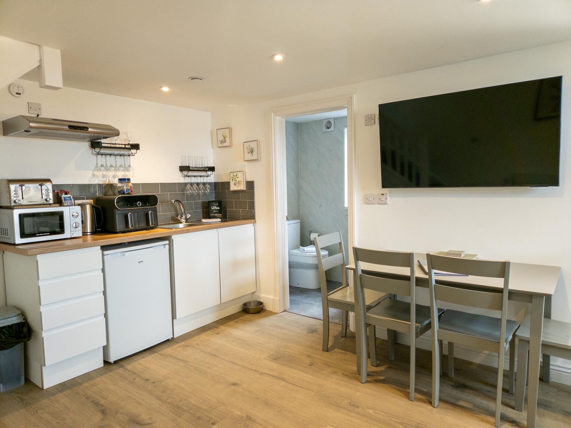 Una cocina compacta con electrodomésticos modernos, un comedor con mesa y sillas, y un televisor montado en la pared.