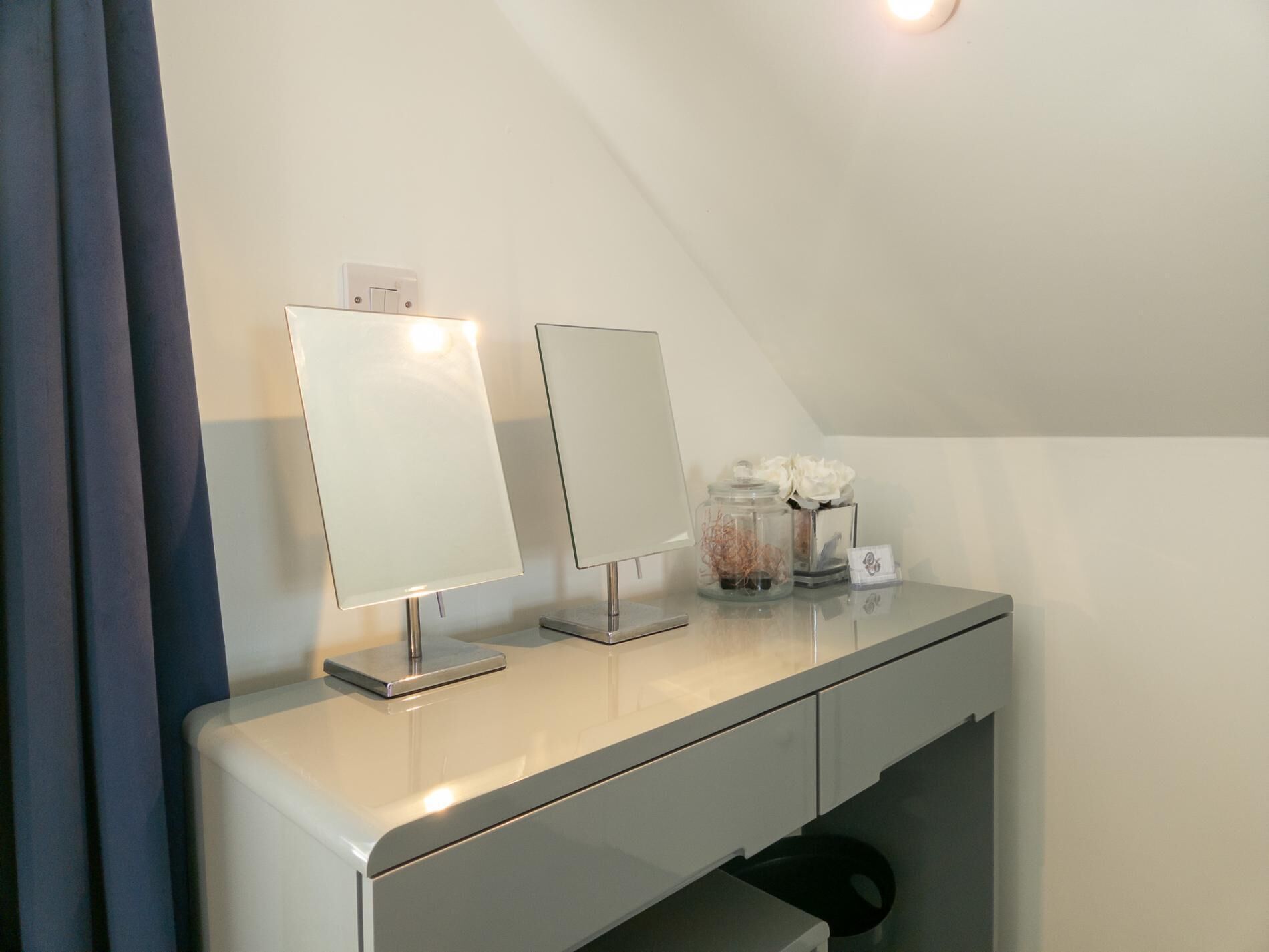 Ein modernes, helles Zimmer mit weißem Schreibtisch, zwei Spiegeln und einem kleinen dekorativen Gegenstand an der Wand.