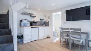 Cocina compacta con electrodomésticos modernos, comedor con mesa y sillas, y una escalera que sube a otro nivel.