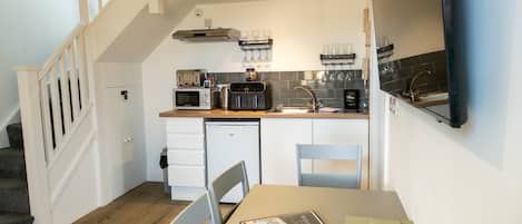 Eine kleine Küche mit Mikrowelle, Toaster und Kaffeemaschine auf der Arbeitsplatte, einem kleinen Kühlschrank und einem Spülbecken mit Weingläsern darüber.