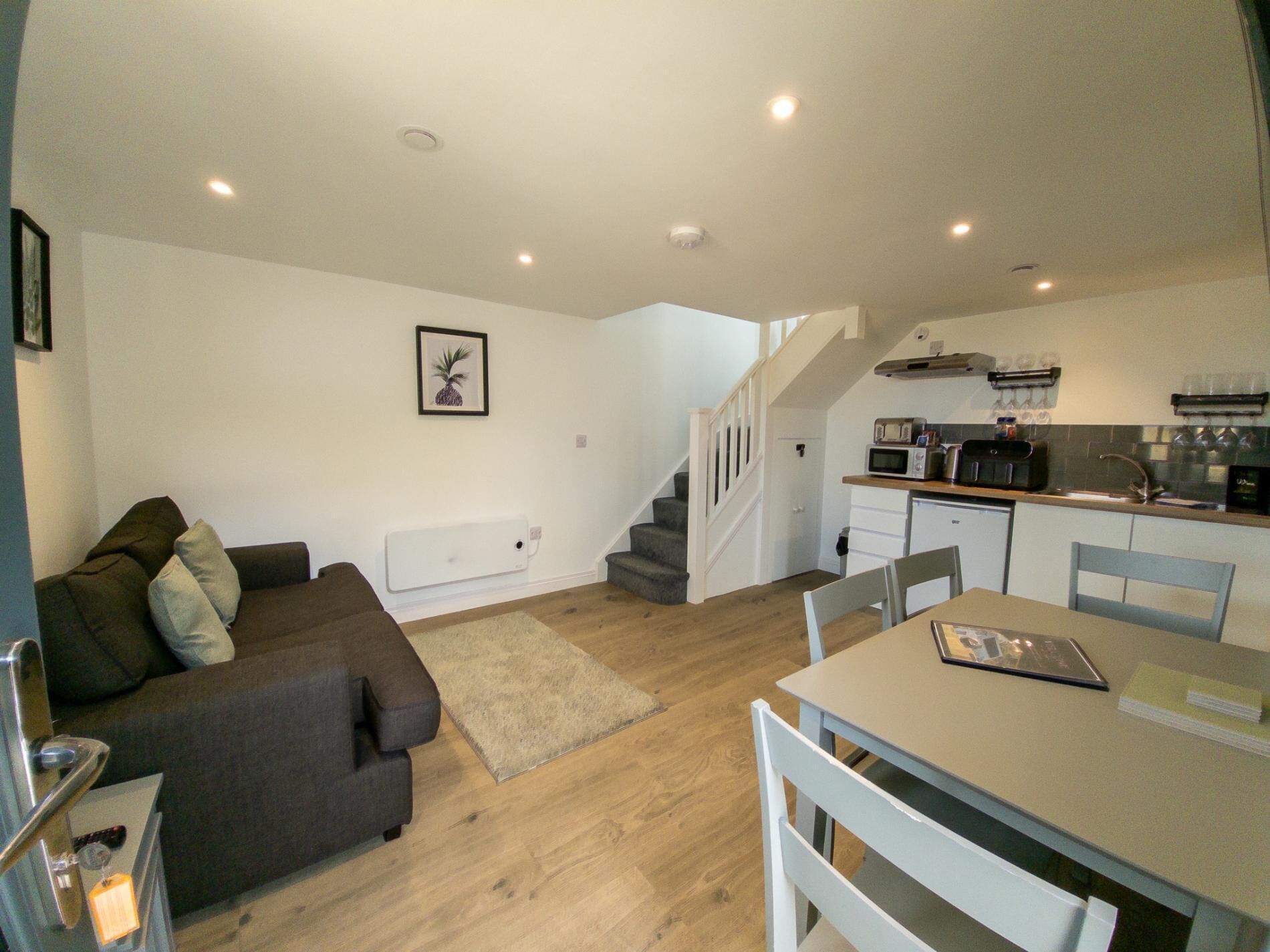 A compact living space with a sofa, a dining table, and a kitchen area including a microwave and sink.