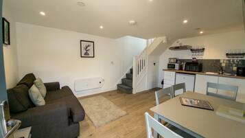 A compact living space with a sofa, a dining table, and a kitchen area including a microwave and sink.