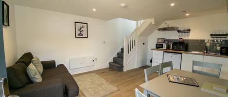 A compact living space with a sofa, a dining table, and a kitchen area including a microwave and sink.