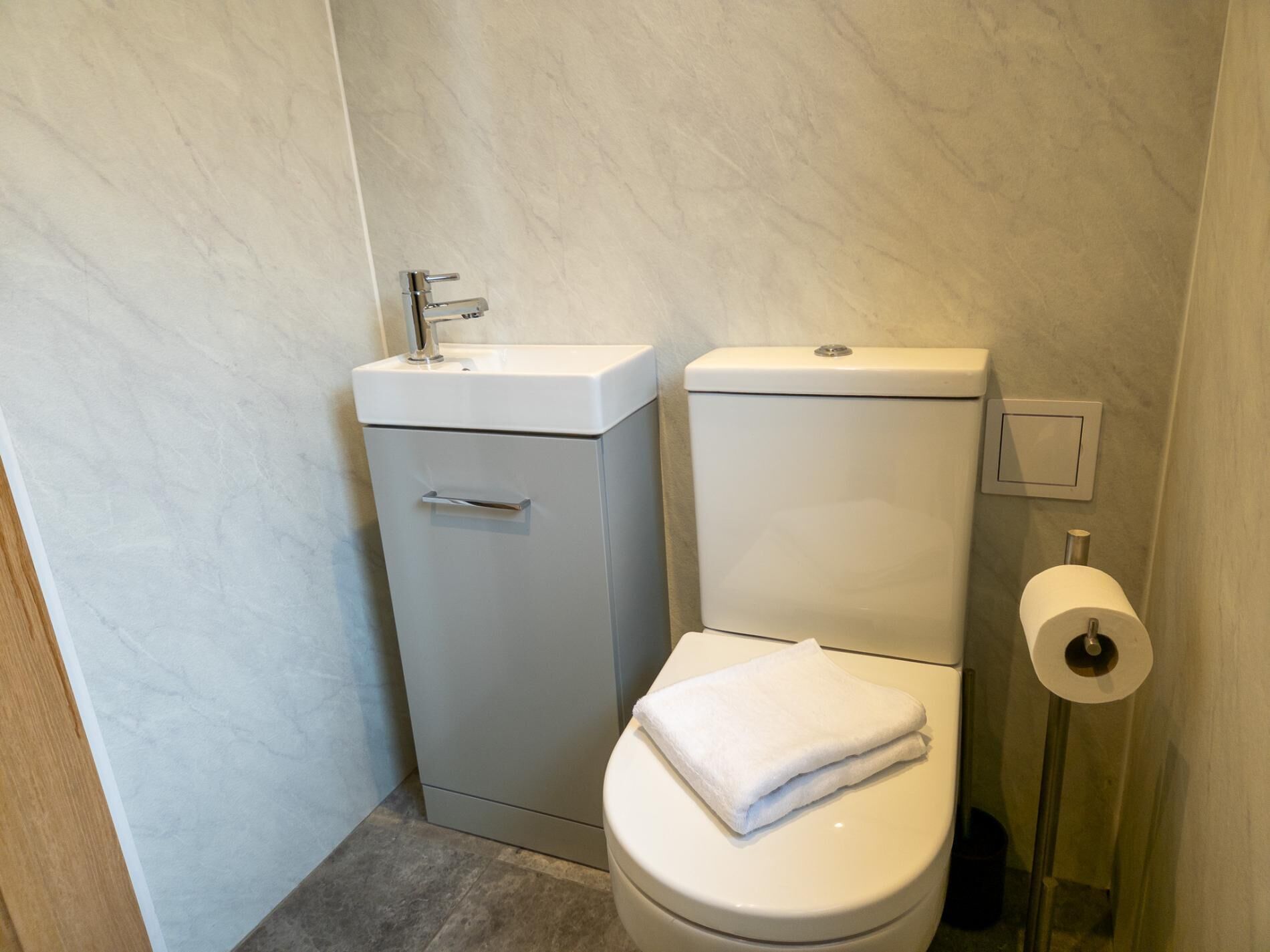 A compact bathroom with a toilet, sink, and toilet paper holder.