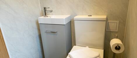 A compact bathroom with a toilet, sink, and toilet paper holder.