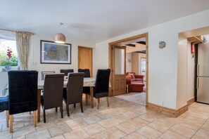 A dining area with a table and chairs, a map on the wall, and a view into another room. - Bullcroft - 6 Bedroom House - Oxwich (Swansea)
