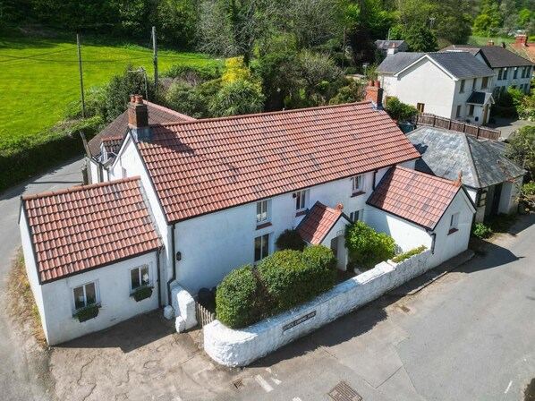 A white building with a red-tiled roof, surrounded by greenery and other buildings. - Bullcroft - 6 Bedroom House - Oxwich (Swansea)