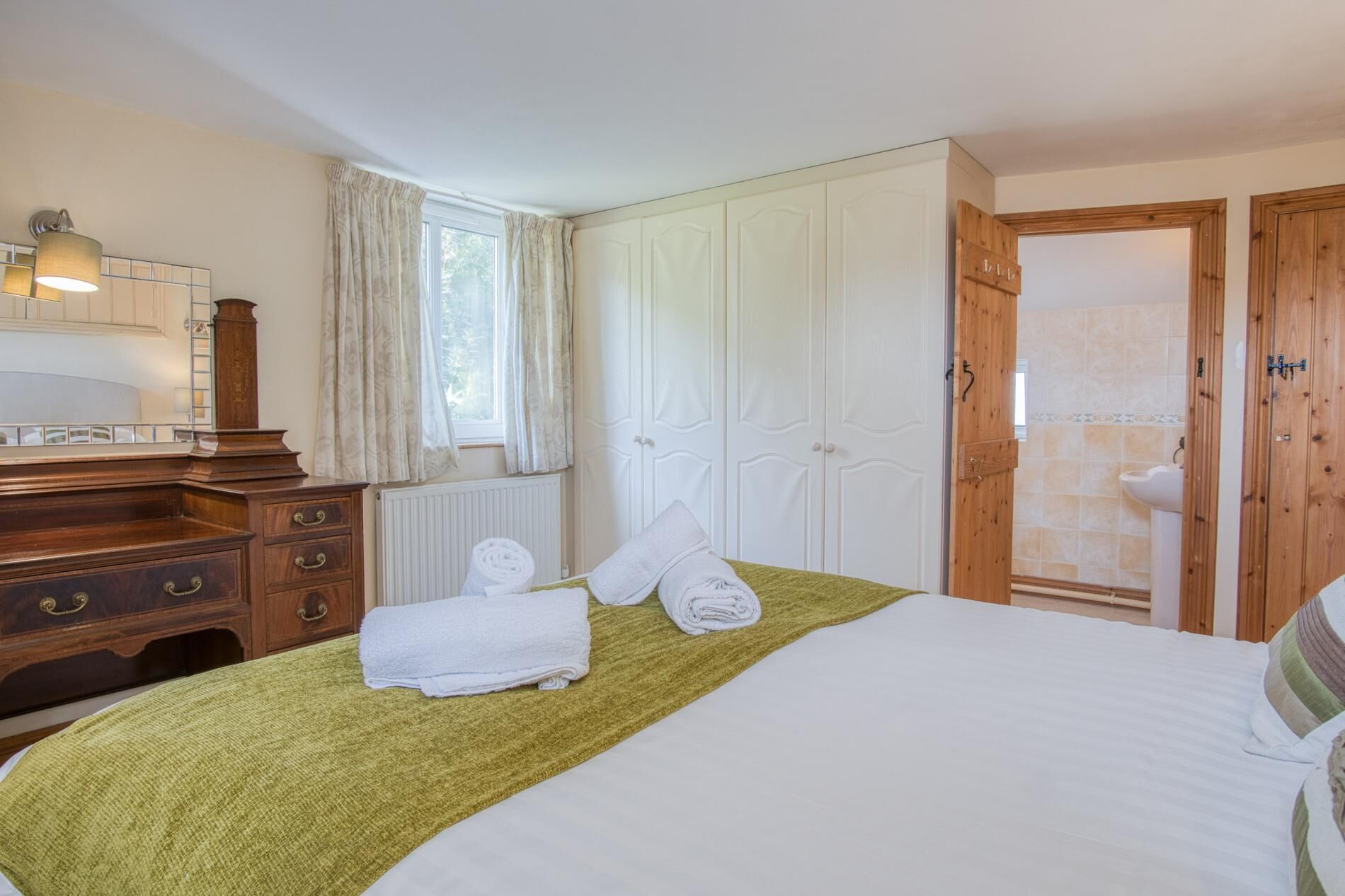 A neatly arranged bedroom with a bed, a wooden dresser, a radiator, and a wooden wardrobe.