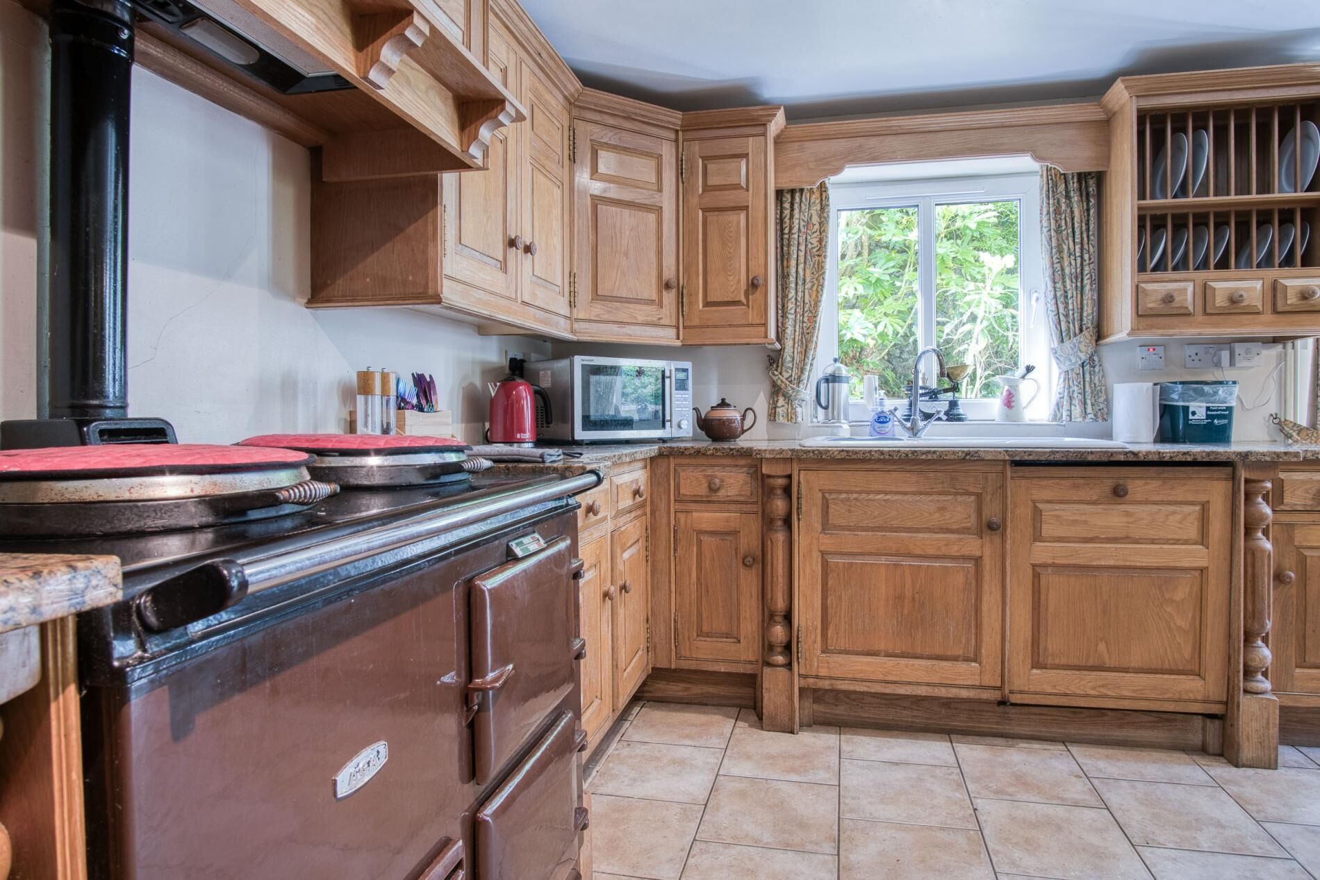 Une cuisine avec des meubles de rangement en bois, une cuisinière, un four à micro-ondes et une fenêtre avec des rideaux.