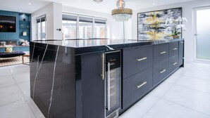 A modern kitchen with a black marble island, pendant lights, and a large abstract painting.