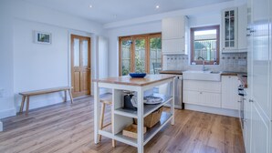 Una cocina moderna con armarios blancos, una mesa de madera y ventana con vista a un jardín.