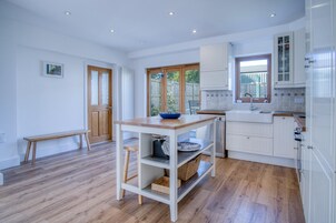 Una cocina moderna con armarios blancos, una mesa de madera y ventana con vista a un jardín.
