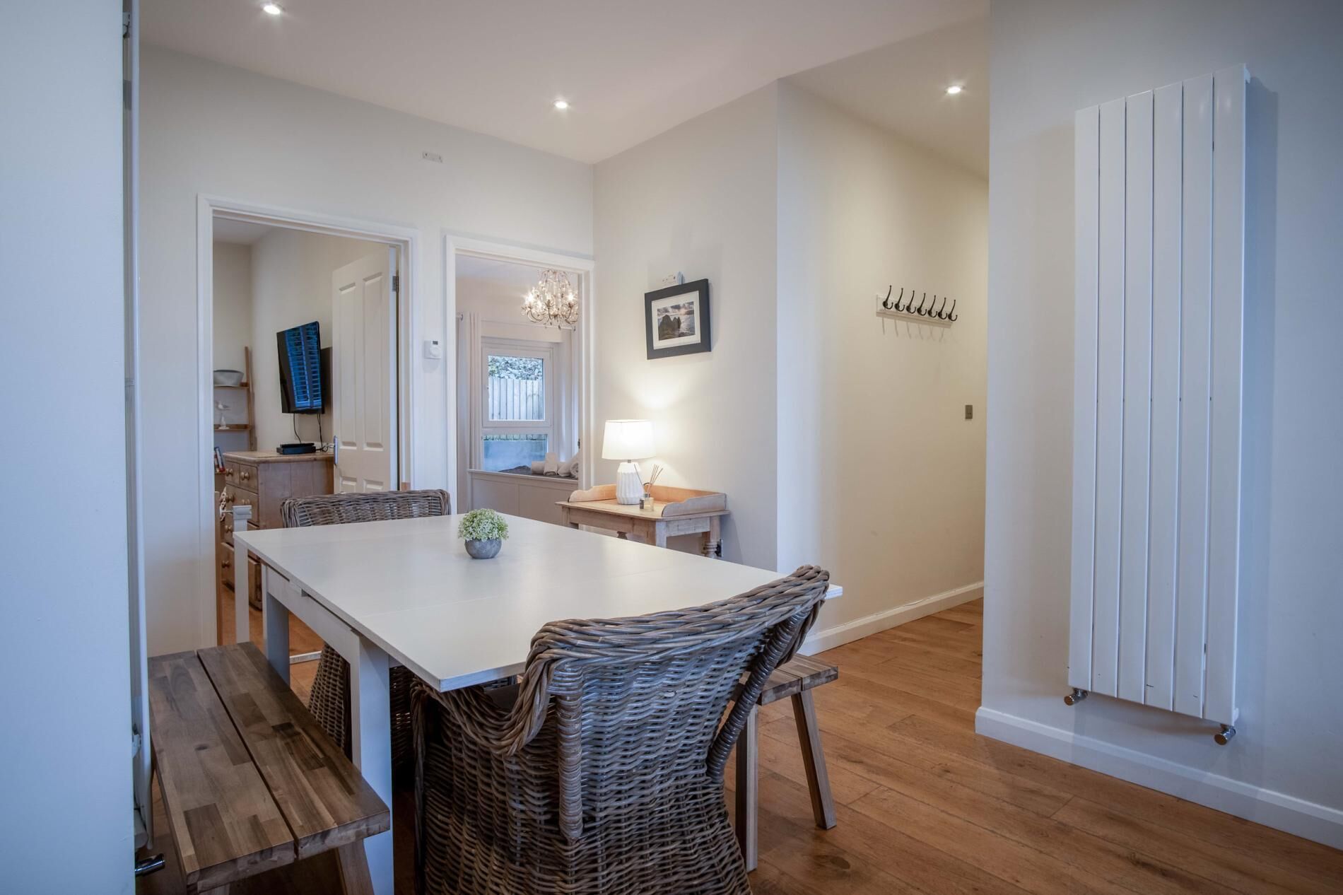 Un coin repas avec une table blanche, des chaises en osier, un banc en bois, un lustre et un tableau accroché au mur.