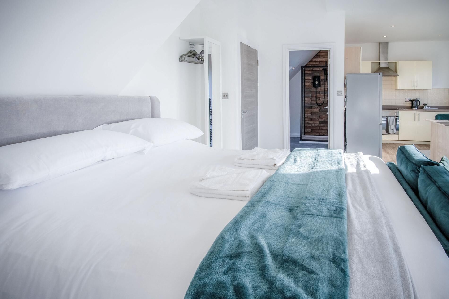 A modern hotel room with a large bed, a bathroom with a shower, and a kitchenette.