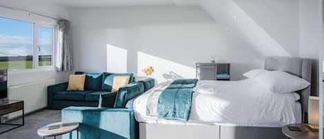 Quarto moderno com uma cama grande, um sofá, uma mesinha e uma mesa de cabeceira.