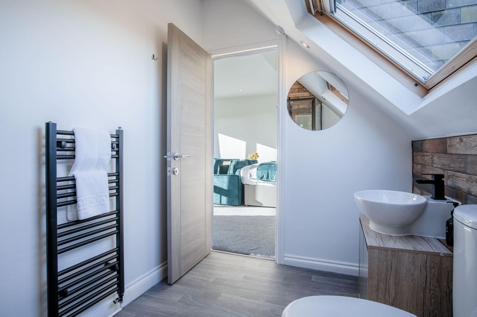 A modern bathroom with a skylight, a towel rack, a sink, and a view of a living area.