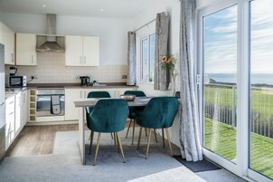A modern kitchen with white cabinets, a built-in oven, and a dining area with teal chairs and a wooden table.