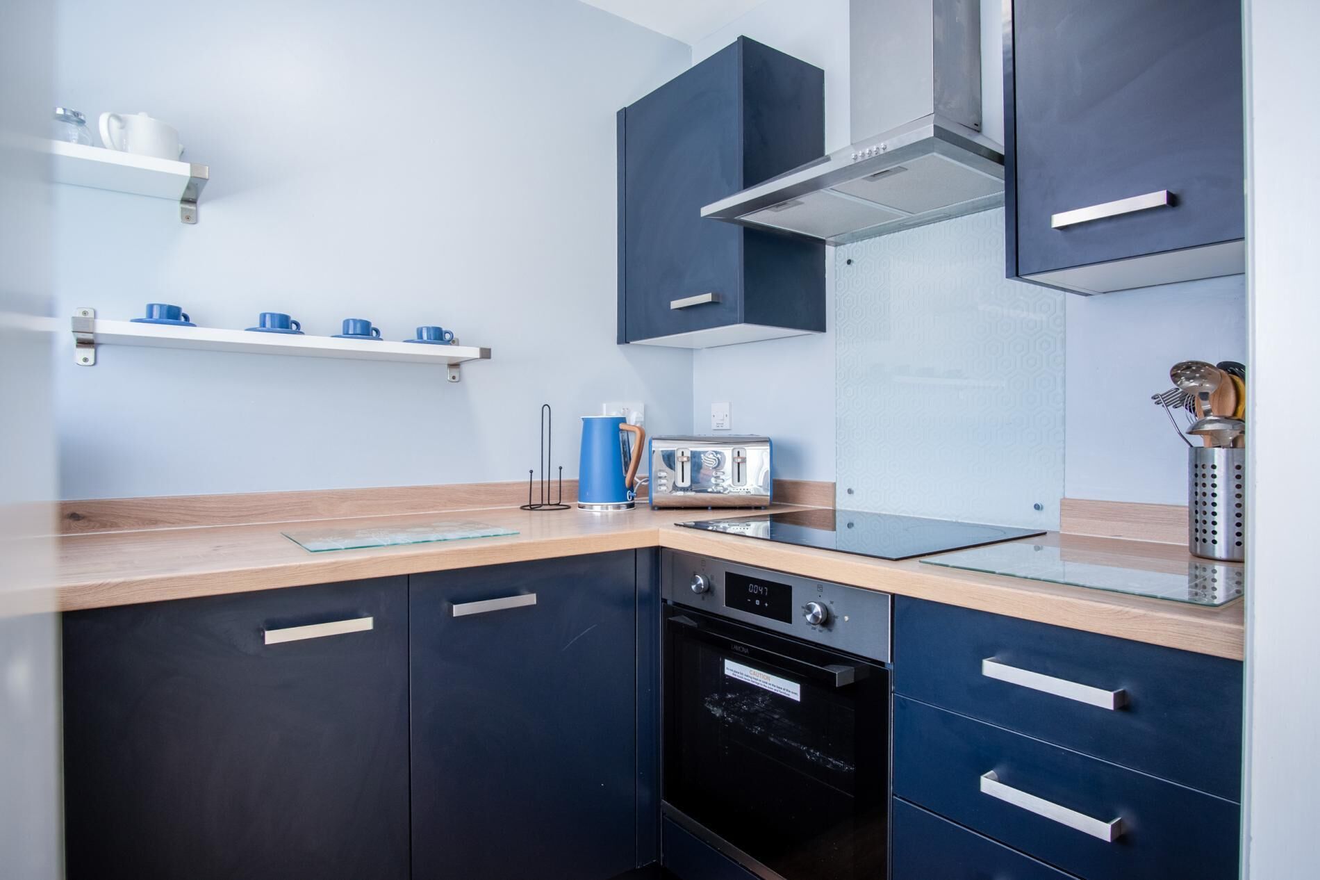 A modern kitchen with dark cabinetry, a stainless steel range hood, and a built-in dishwasher.