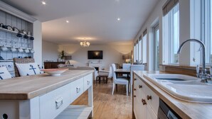 Una cocina moderna con una isla central, un comedor con mesa y sillas, y un amplio ventanal que proporciona luz natural.
