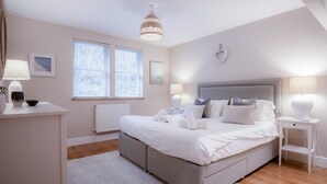 Un dormitorio con cama, mesitas de noche, un radiador y una ventana con persianas.