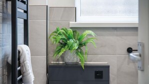 A bathroom with a towel hanging on a rack, a potted plant on a cabinet, and a toilet with a flush handle. - Bayview 58 - 2 Bedroom Chalet - Bayview Oxwich (Swansea)