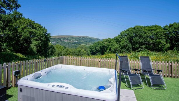 Ein Whirlpool mit Holzzaun und Liegestühlen in einem Garten mit Blick auf Hügel.