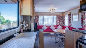 Eine kleine Küche mit Spüle, ein Essbereich mit rotem Sofa und Stühlen sowie ein großes Fenster mit Vorhängen.