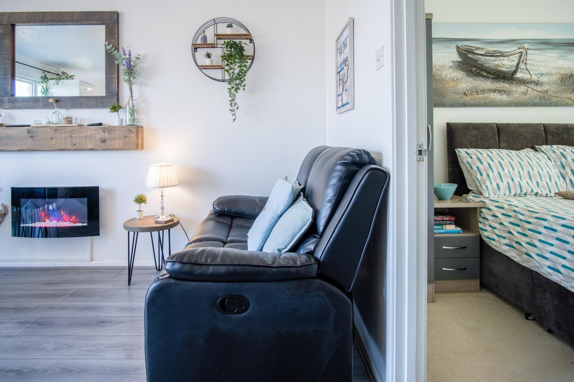 Un salon moderne doté d’un fauteuil massant, d’un téléviseur à écran plat, d’une petite table d’appoint avec une lampe et d’une étagère murale agrémentée de plantes.